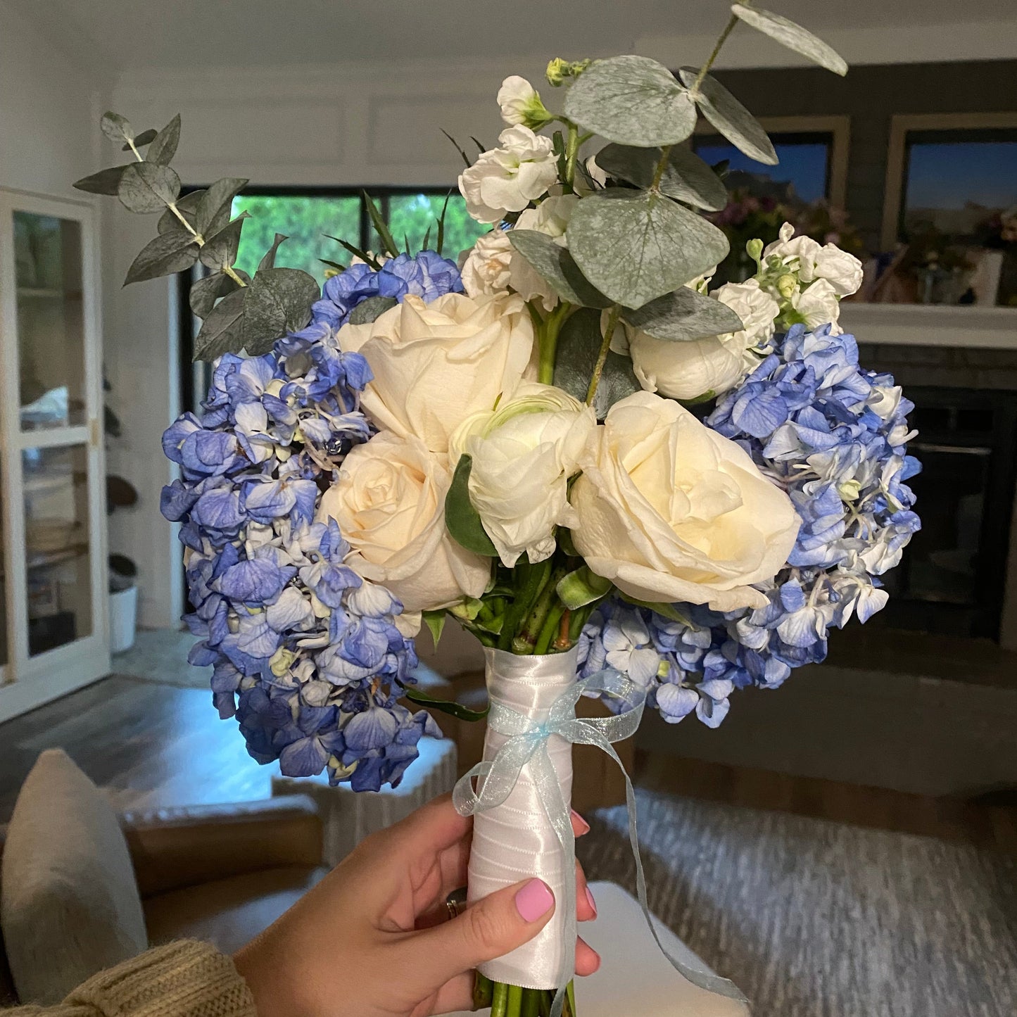 Bouquet of blue and white flowers held by a person indoors.