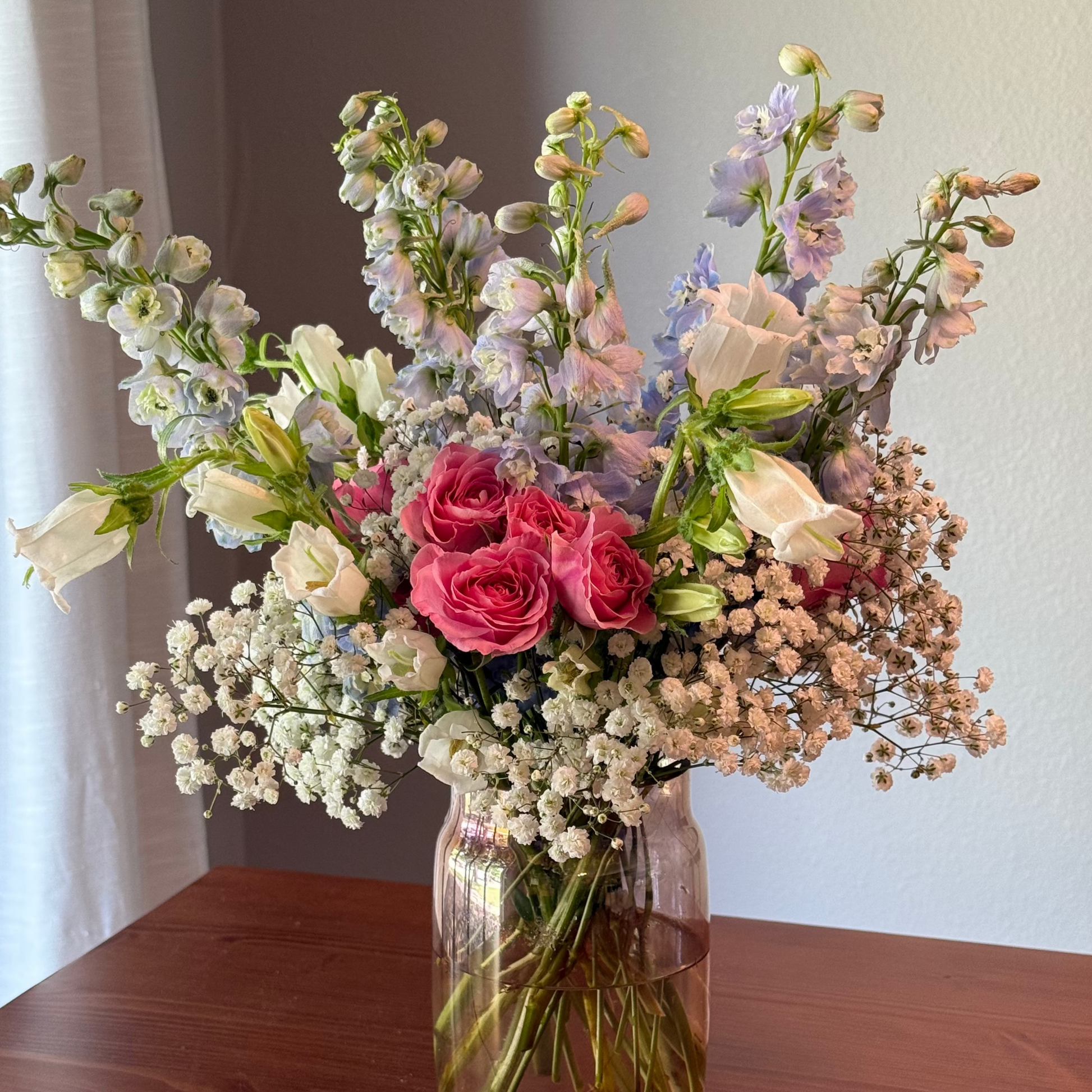 Bouquet of pink and blue garden-style flowers in a clear vase.